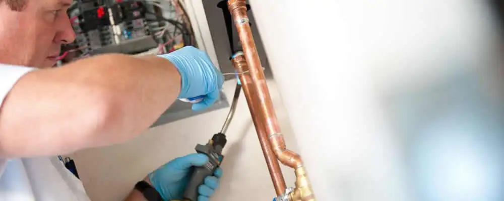 Water heater repair technician testing copper pipe connections and controls in Long Beach, CA